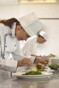 Female chef preparing plates of food, female cook in background